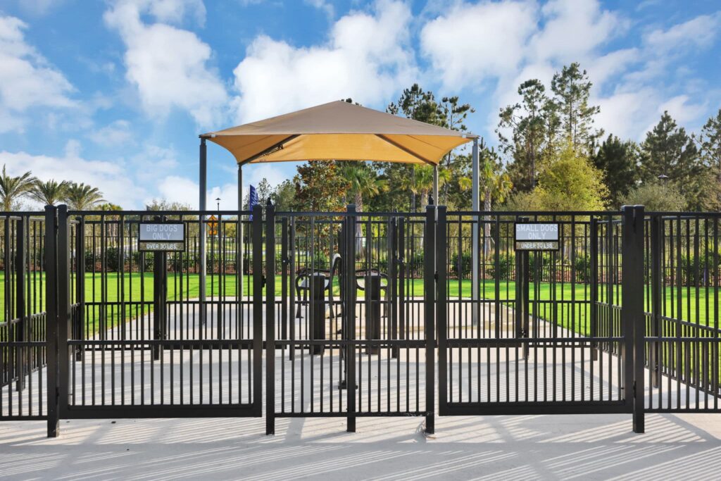 Fenced dog park entry gates with shade canopy at Skipping Stone